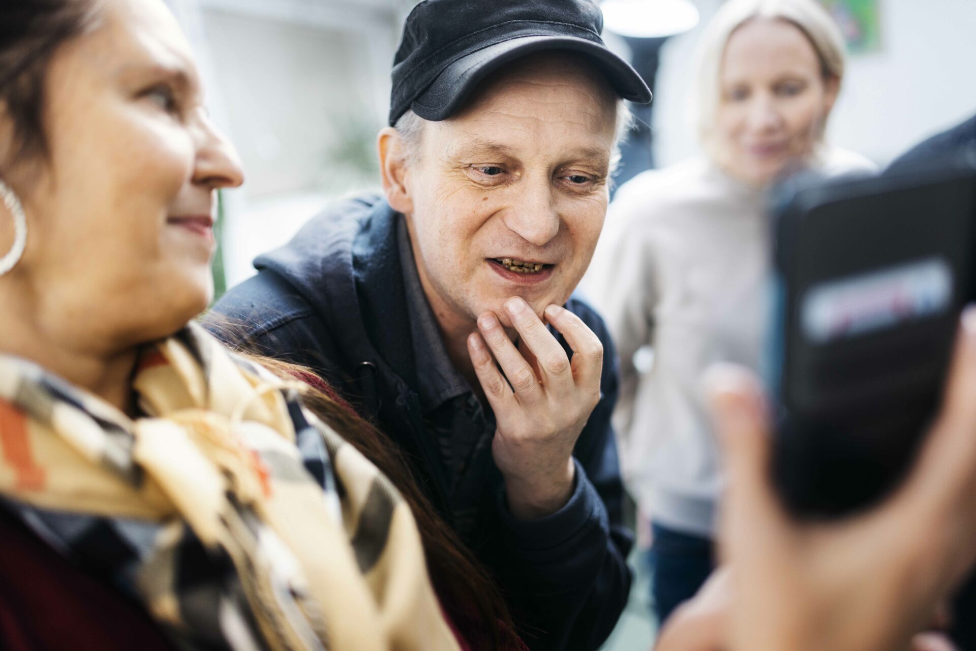 Kolme ihmistä, mies kahden naisen keskellä, katsovat puhelinta pohtien ja oivaltaen.