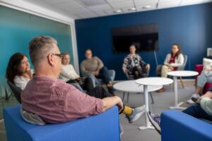 Kuusi ihmistä istuu sinisävyisessä toimistossa keskustelemassa. Kasvoja ei erota selkeäsi.