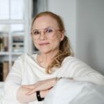 Kuvassa nainen istuu tuolilla ja katsoo kameraan.